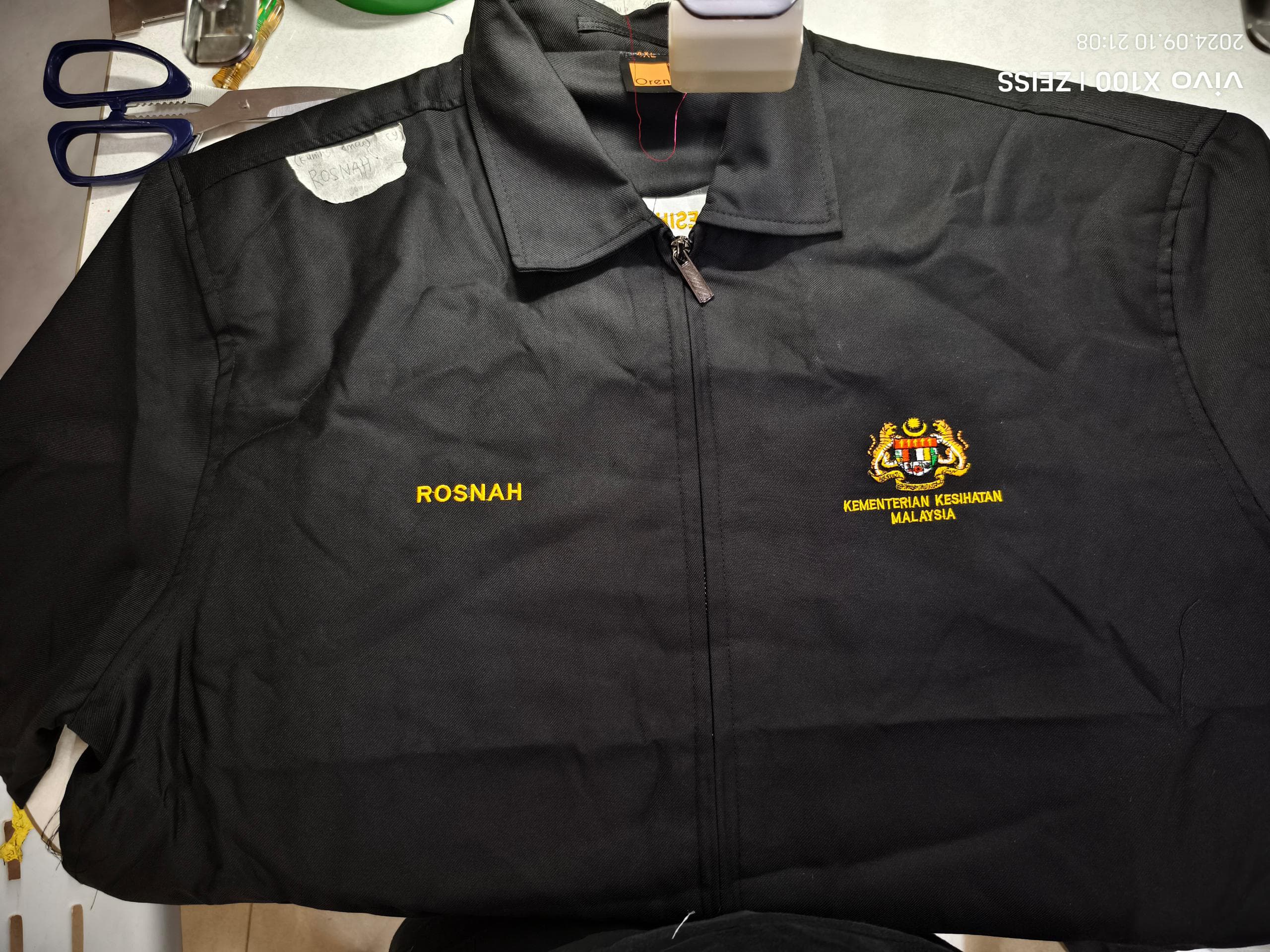 Jaket hitam dengan sulaman Kementerian Kesihatan Malaysia dan nama Rosnah