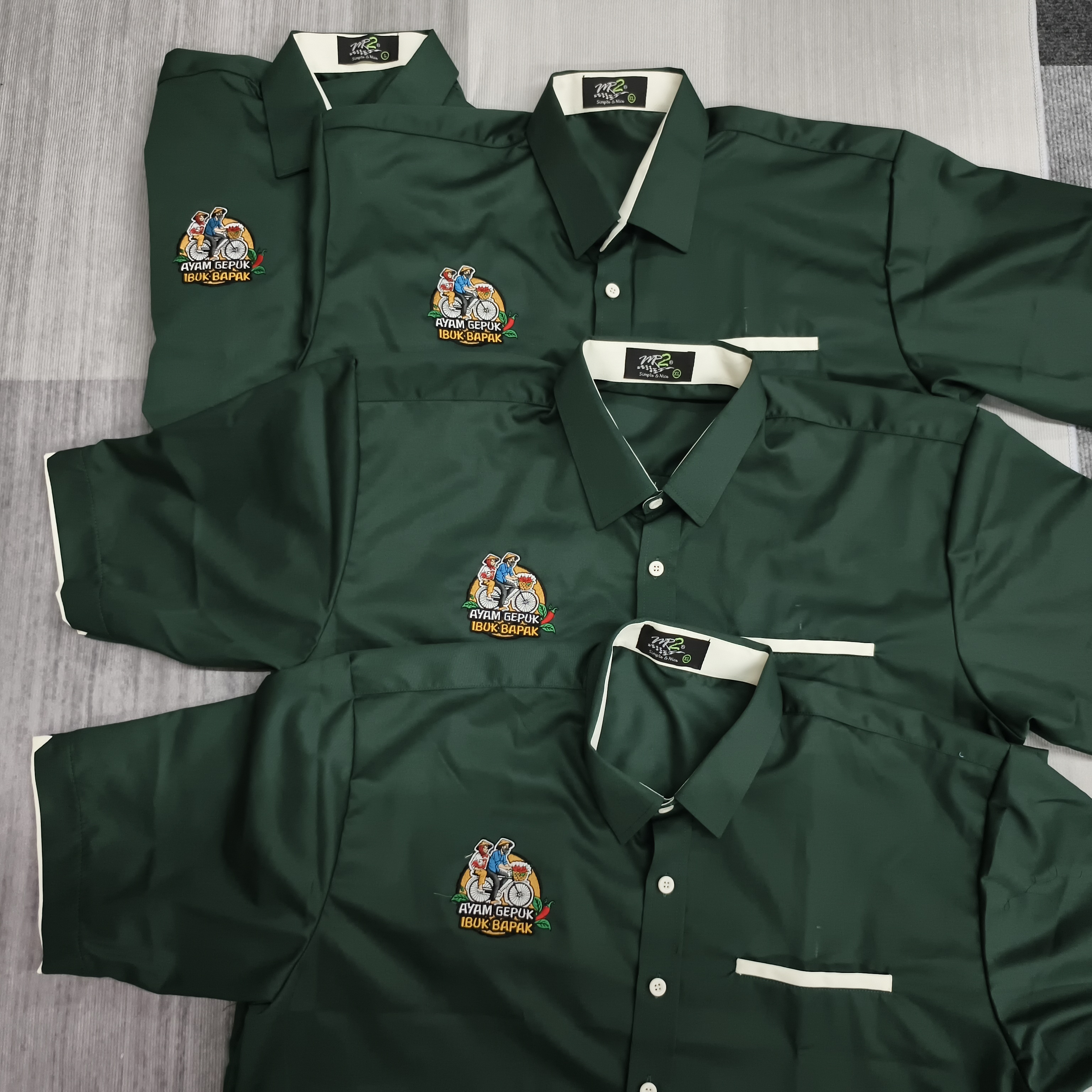 Uniform hijau dengan sulaman logo Ayam Gepuk Ibuk Bapak pada bahagian dada