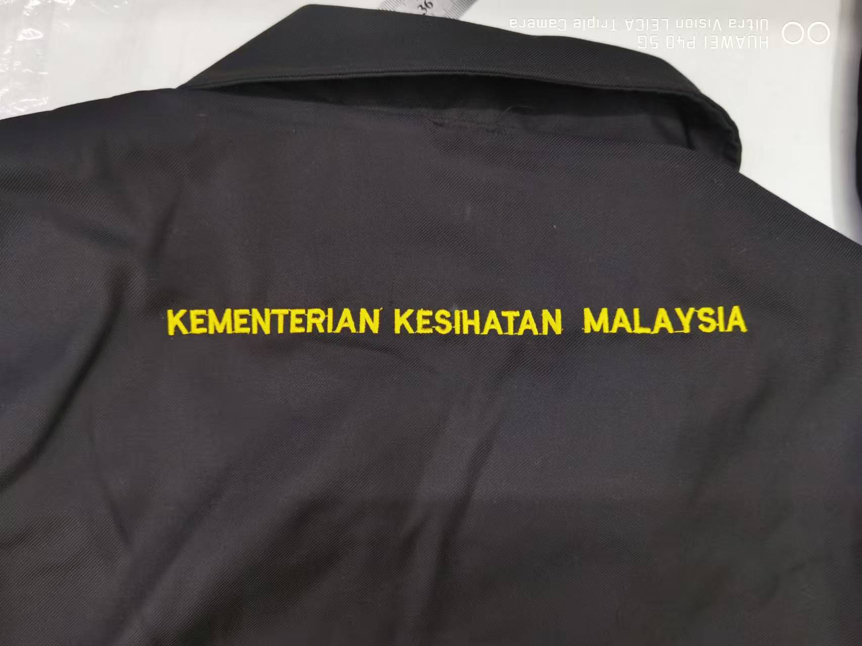 Tulisan sulaman kuning Kementerian Kesihatan Malaysia pada belakang jaket hitam
