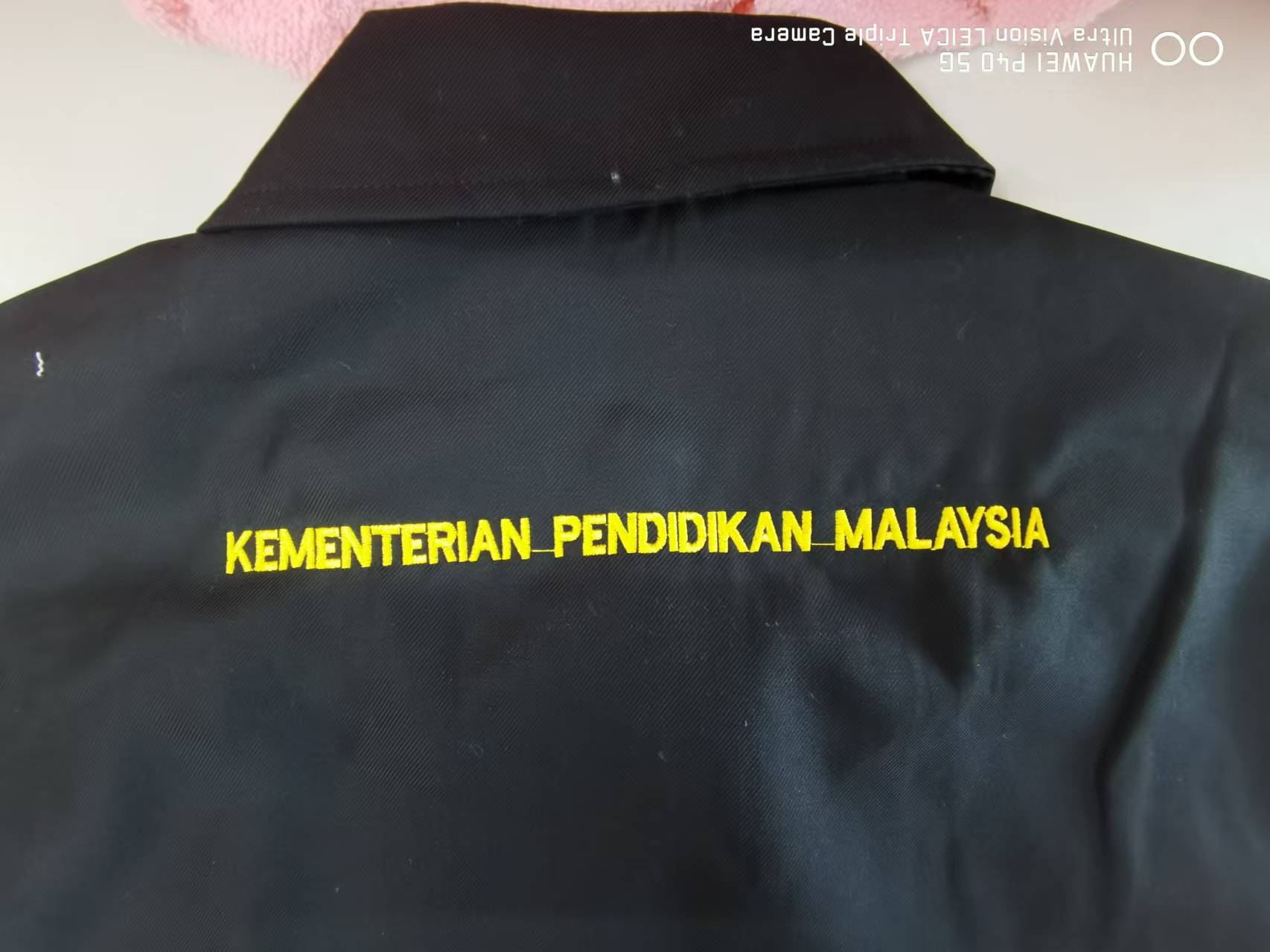 Tulisan sulaman kuning Kementerian Pendidikan Malaysia pada belakang jaket hitam